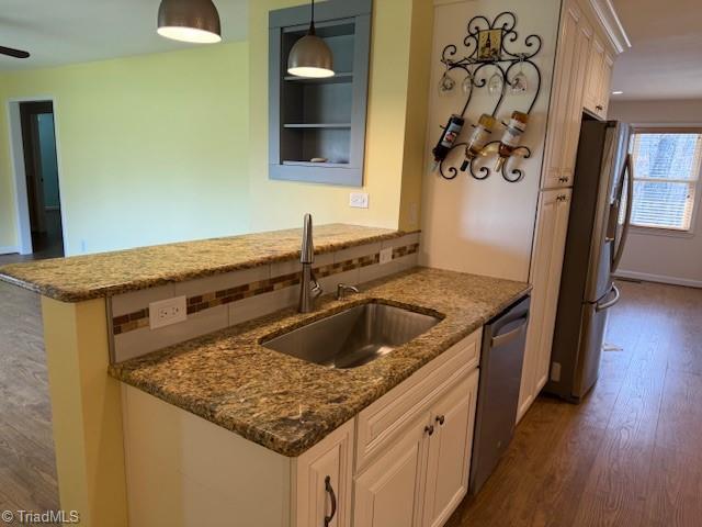 kitchen with a sink, dark stone countertops, tasteful backsplash, dark wood-style floors, and appliances with stainless steel finishes