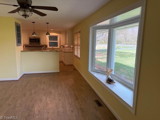 kitchen with stainless steel microwave, visible vents, baseboards, decorative light fixtures, and wood finished floors