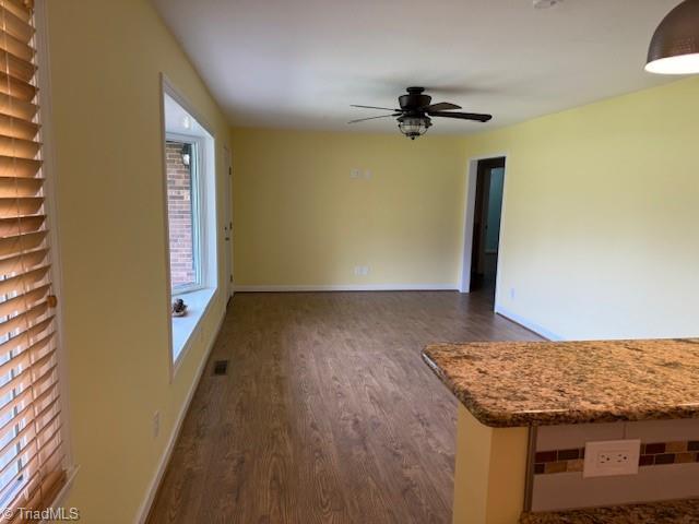 unfurnished living room with dark wood-type flooring, baseboards, and ceiling fan