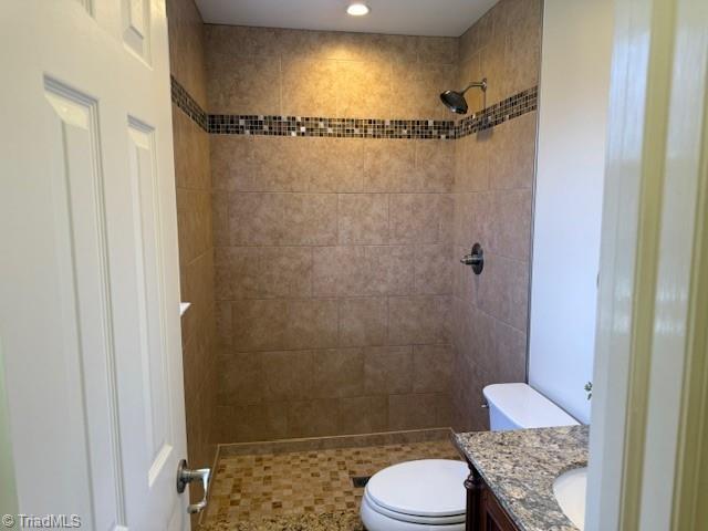 full bathroom featuring tiled shower, toilet, and vanity