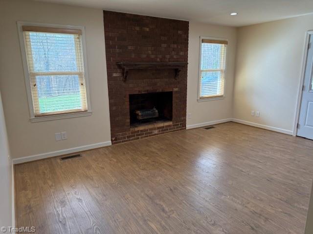 unfurnished living room featuring visible vents, baseboards, and wood finished floors