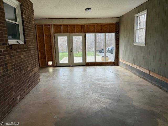 unfurnished room featuring brick wall, french doors, a textured ceiling, and concrete floors