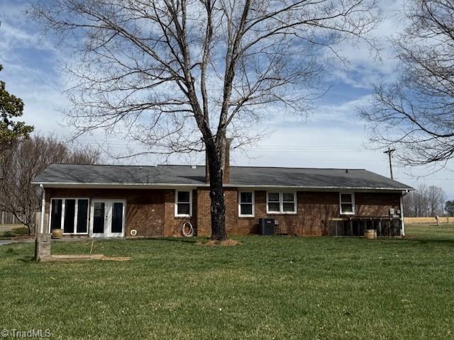 rear view of property featuring a yard, central AC unit, and brick siding