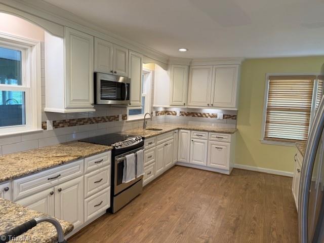 kitchen with light wood finished floors, white cabinets, stainless steel appliances, and tasteful backsplash