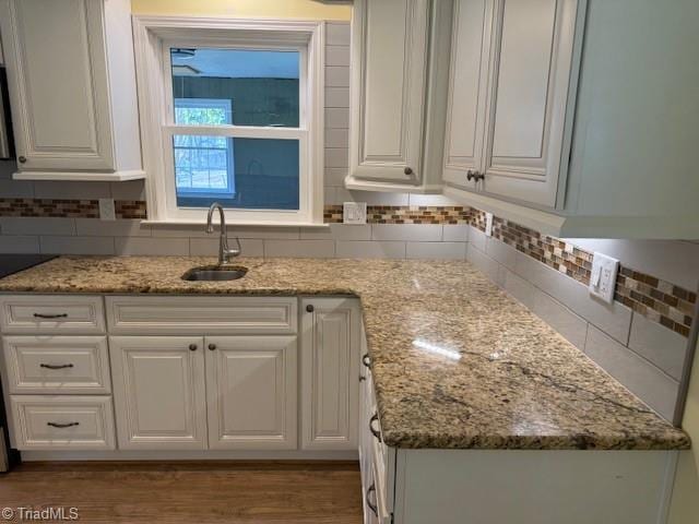 kitchen featuring light stone counters, wood finished floors, a sink, white cabinets, and backsplash