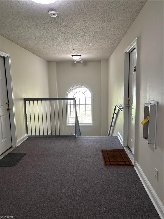 hallway with an upstairs landing, dark carpet, a textured ceiling, and baseboards