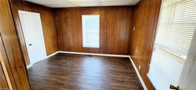 unfurnished room with dark hardwood / wood-style flooring, a drop ceiling, and wooden walls