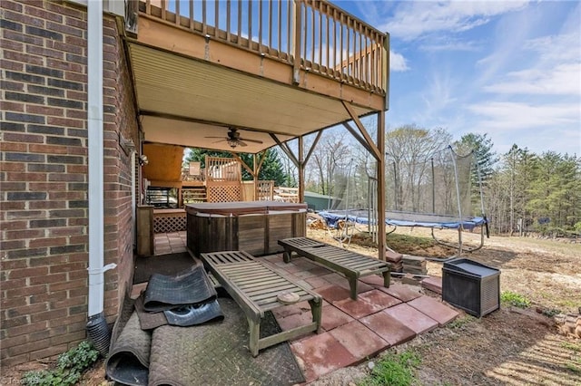 view of patio with a hot tub, a trampoline, a deck, and a ceiling fan