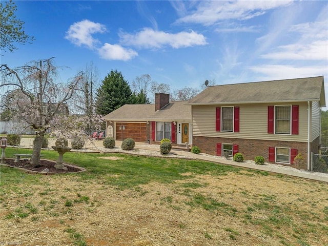 tri-level home featuring a chimney, fence, brick siding, and a front yard