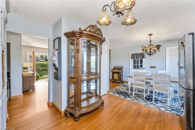 dining area featuring baseboards, a textured ceiling, light wood-style flooring, and a notable chandelier