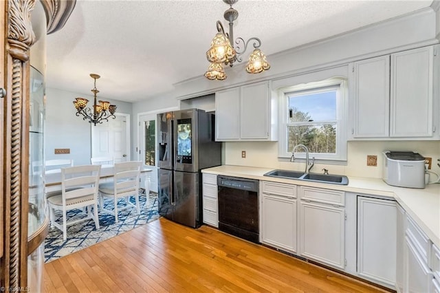 kitchen featuring a sink, a chandelier, light wood-type flooring, stainless steel refrigerator with ice dispenser, and black dishwasher