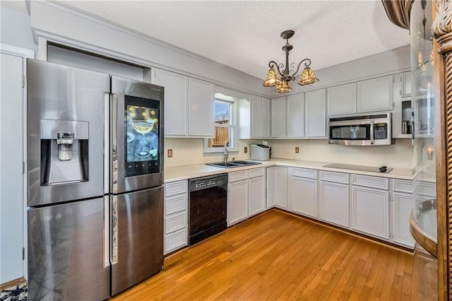 kitchen with light countertops, light wood-type flooring, an inviting chandelier, a sink, and black appliances