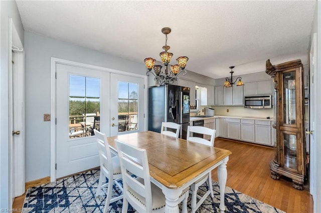 dining area featuring a textured ceiling, light wood-style floors, french doors, and a chandelier