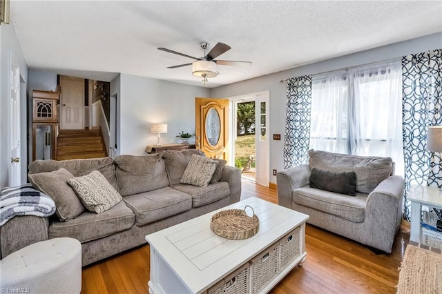 living area featuring a textured ceiling, hardwood / wood-style flooring, stairs, and ceiling fan