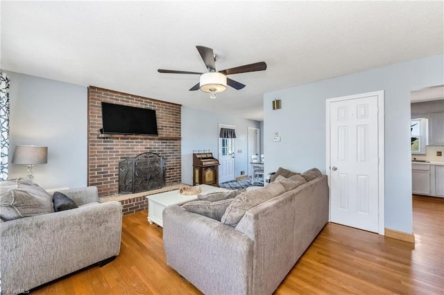 living room featuring a fireplace, light wood-style flooring, ceiling fan, and a textured ceiling