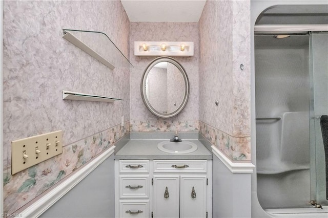 bathroom featuring a shower with shower door, wallpapered walls, and vanity
