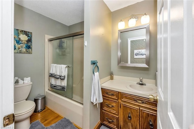 full bathroom featuring a textured ceiling, combined bath / shower with glass door, toilet, wood finished floors, and vanity