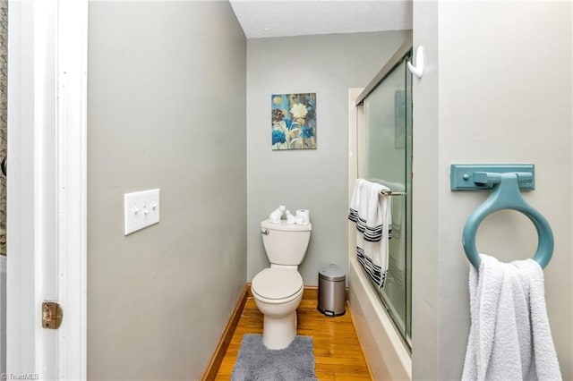 full bath featuring baseboards, wood finished floors, toilet, and bath / shower combo with glass door