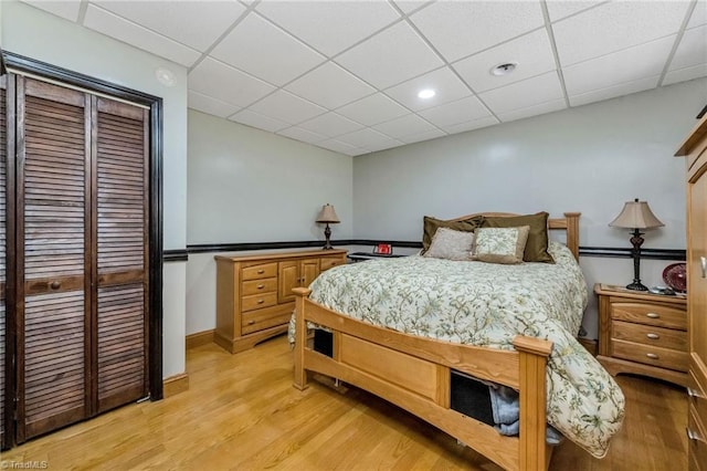 bedroom featuring baseboards, light wood-type flooring, and a paneled ceiling