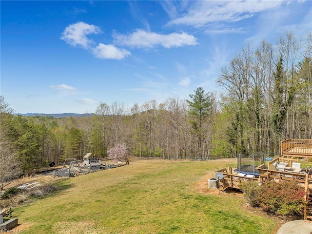 view of yard featuring a deck, a wooded view, and a trampoline