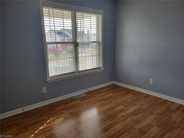 unfurnished room with wood finished floors, visible vents, and baseboards