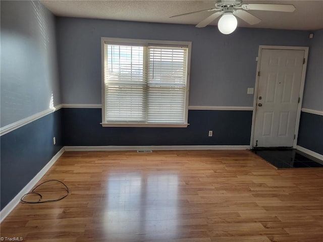 unfurnished room with a textured ceiling, a ceiling fan, baseboards, and wood finished floors