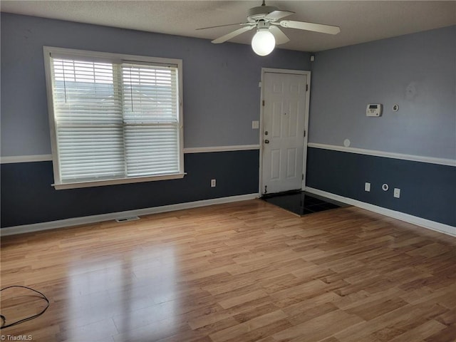 unfurnished room with visible vents, a textured ceiling, wood finished floors, baseboards, and ceiling fan