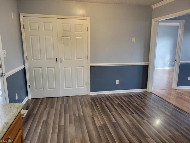 unfurnished bedroom with a closet, baseboards, and dark wood-style flooring