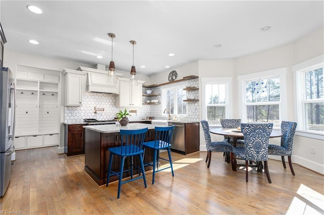 kitchen featuring a center island, appliances with stainless steel finishes, decorative backsplash, open shelves, and light wood finished floors