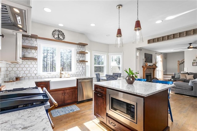 kitchen featuring a fireplace, open shelves, stainless steel appliances, a sink, and light wood-type flooring