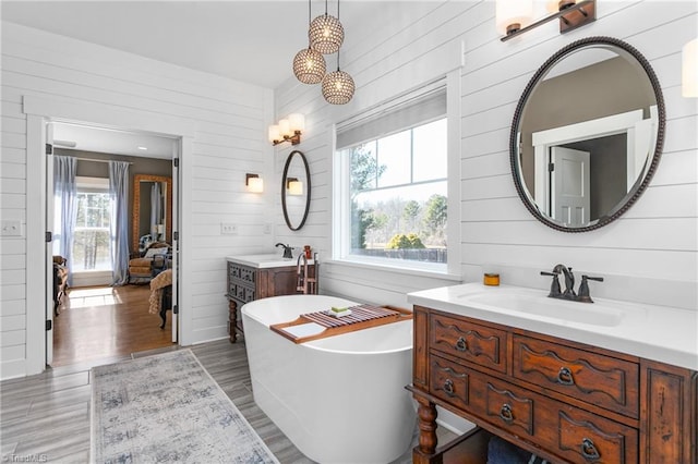 bathroom with a freestanding bath, two vanities, a sink, and wood finished floors