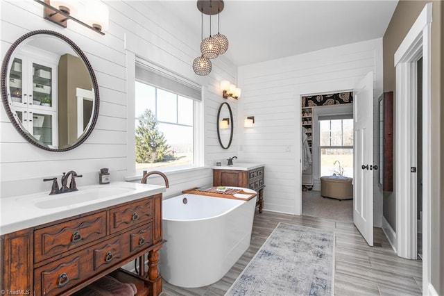 full bathroom featuring a freestanding bath, two vanities, a sink, and a wealth of natural light