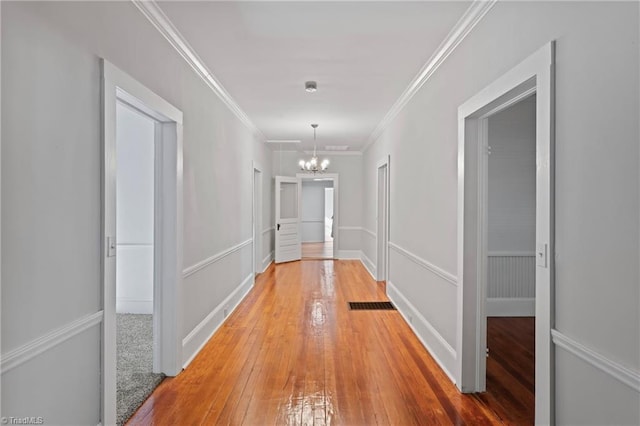 hall with wood-type flooring, crown molding, and a notable chandelier