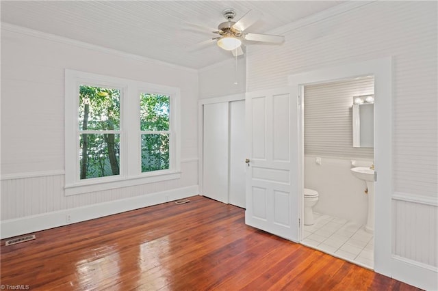 unfurnished bedroom featuring ensuite bathroom, ceiling fan, wood-type flooring, and ornamental molding