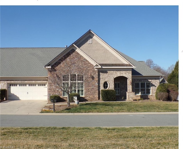 craftsman house with a front yard, driveway, an attached garage, stone siding, and brick siding