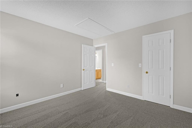 unfurnished room with dark carpet, attic access, a textured ceiling, and baseboards