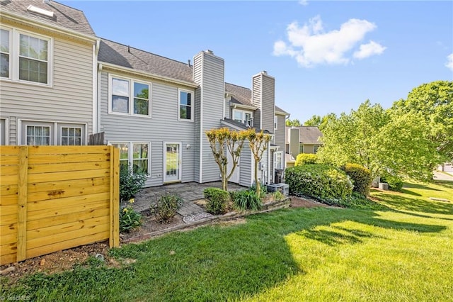 back of property with fence, cooling unit, a chimney, a patio area, and a yard