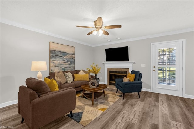 living room featuring ceiling fan, crown molding, a tile fireplace, wood finished floors, and baseboards