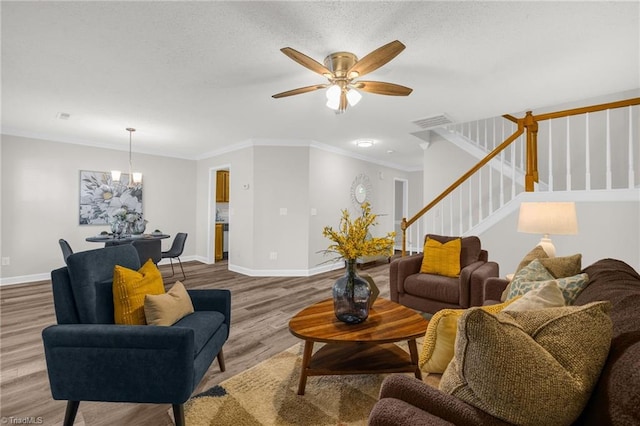 living room featuring visible vents, stairs, wood finished floors, baseboards, and ceiling fan with notable chandelier