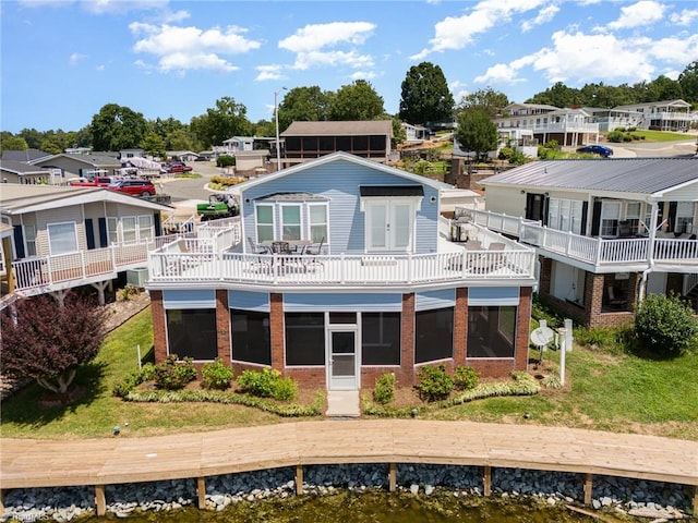 back of property with a balcony, a sunroom, and a lawn