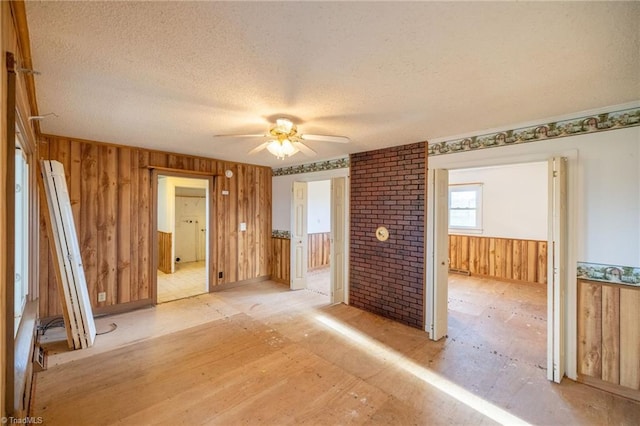 empty room with a textured ceiling, ceiling fan, and wood walls