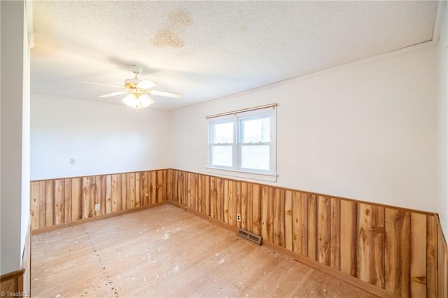 unfurnished room with ceiling fan, a textured ceiling, wooden walls, and light hardwood / wood-style flooring