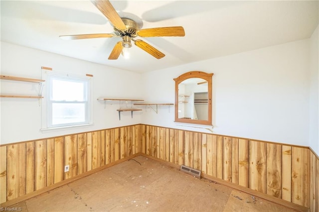 empty room featuring ceiling fan and wooden walls