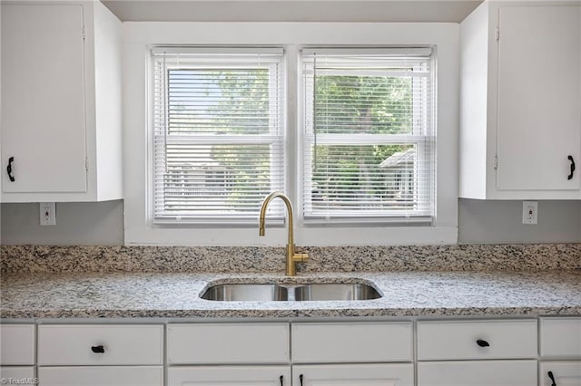 kitchen featuring light stone counters, sink, a healthy amount of sunlight, and white cabinets