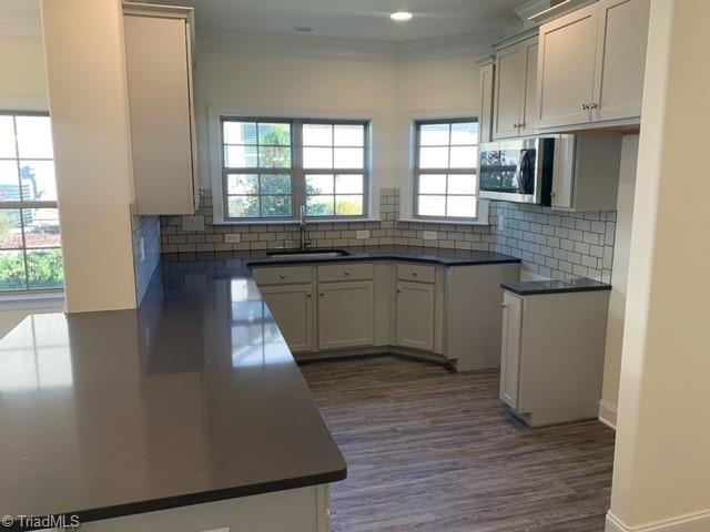 kitchen with dark hardwood / wood-style flooring, backsplash, crown molding, sink, and white cabinets