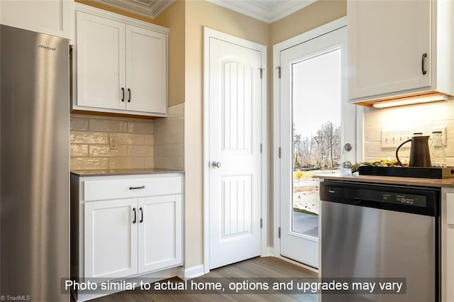 kitchen with stainless steel appliances, dark wood finished floors, ornamental molding, white cabinets, and backsplash