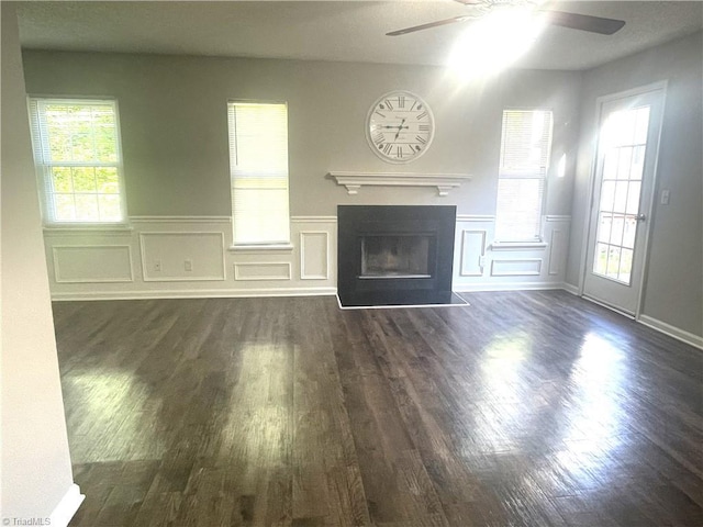 unfurnished living room featuring ceiling fan, a decorative wall, and dark wood-style floors