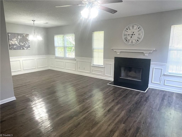 unfurnished living room with dark wood finished floors, ceiling fan with notable chandelier, a decorative wall, and a glass covered fireplace