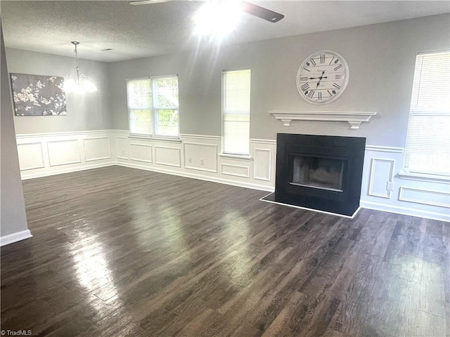 unfurnished living room featuring a fireplace, wainscoting, ceiling fan with notable chandelier, and a decorative wall