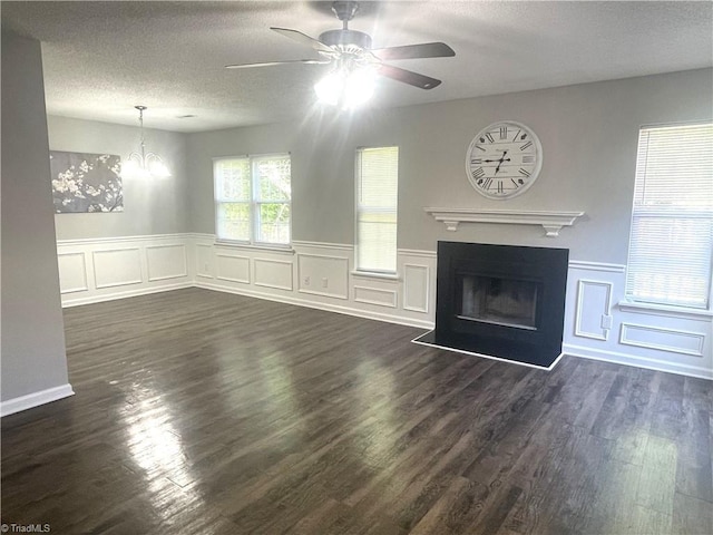unfurnished living room with a textured ceiling, ceiling fan with notable chandelier, and a decorative wall
